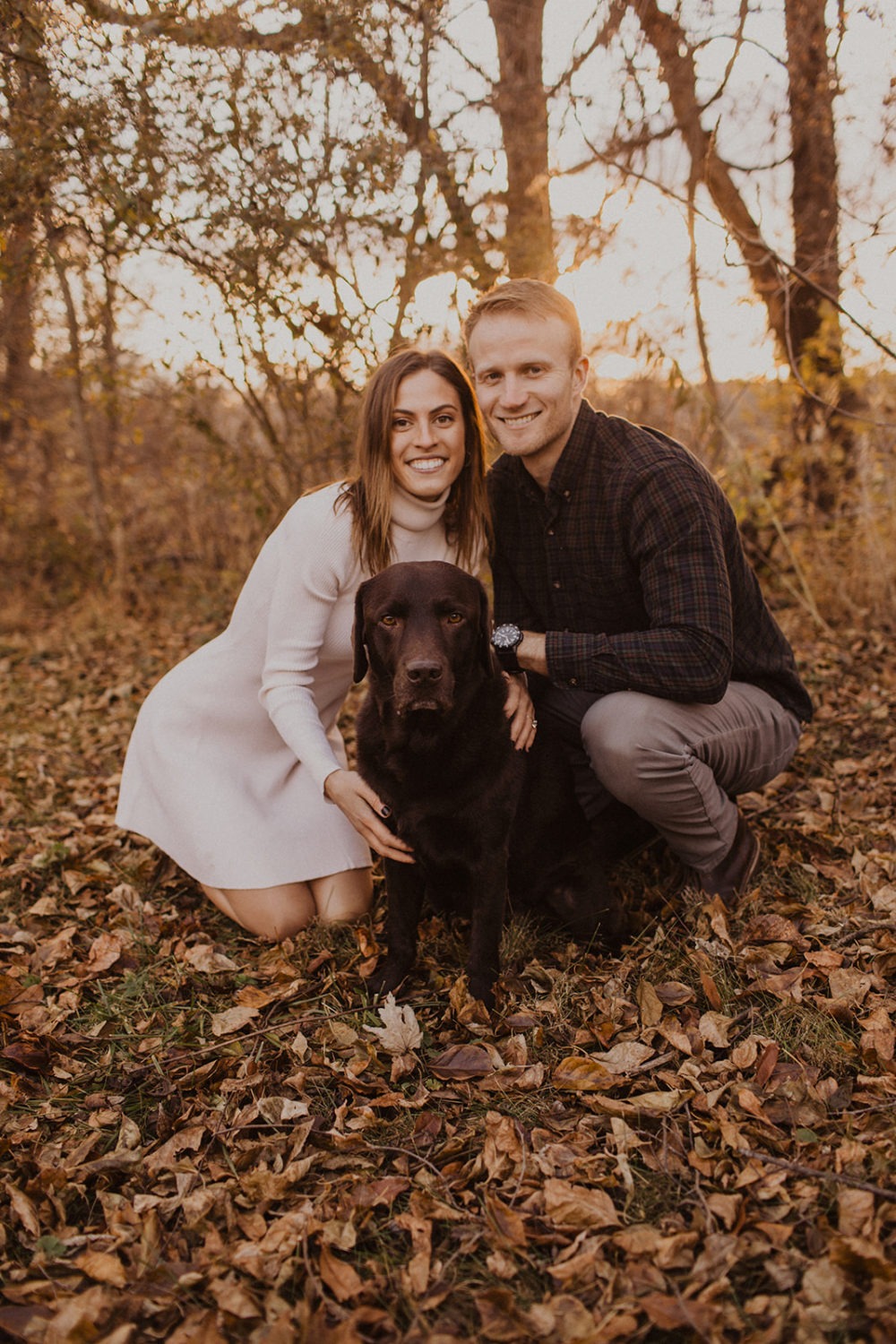 couple sits on falls leaves at outdoor fall engagement photos session with dog