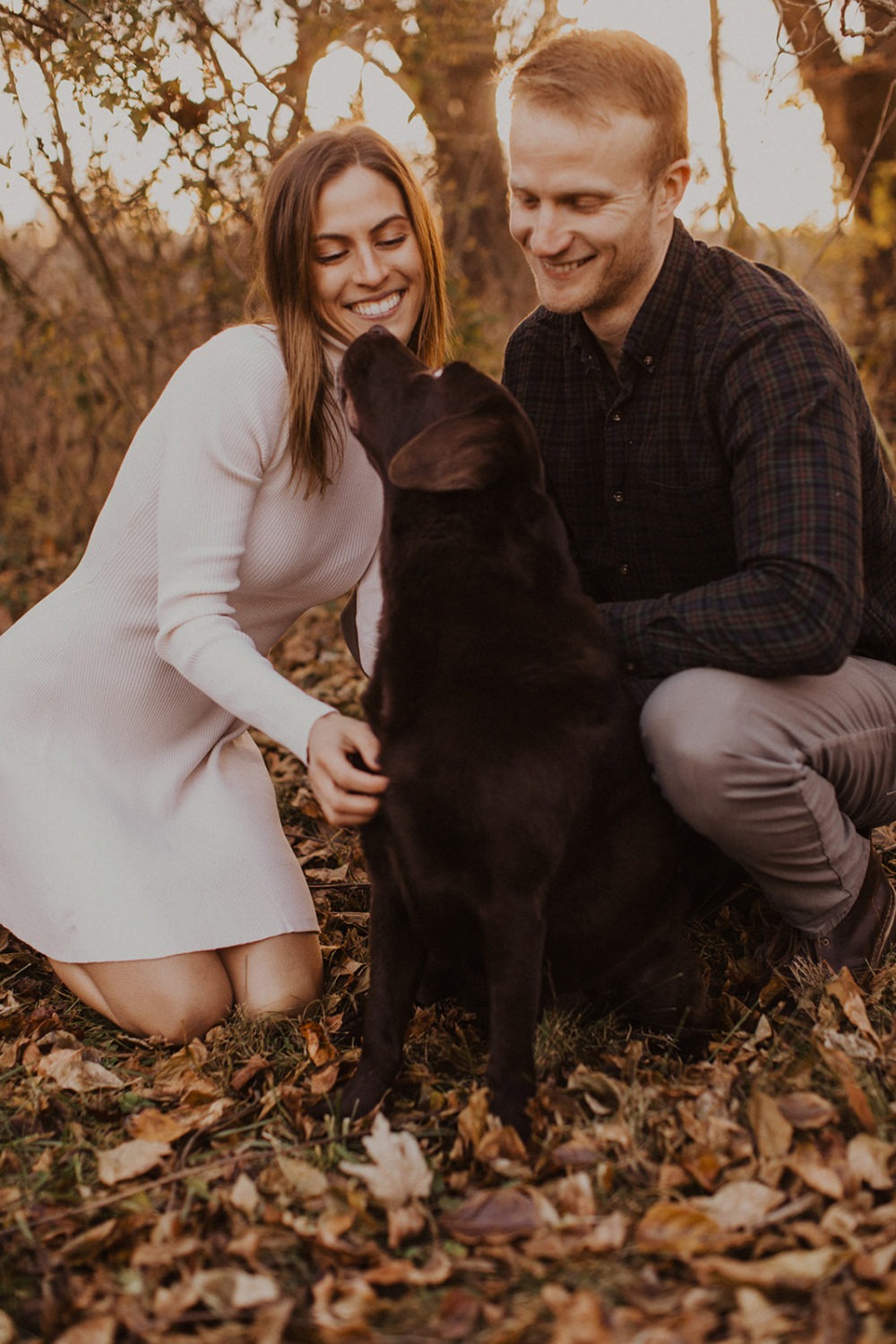 couple sits on falls leaves at outdoor fall engagement photos session with dog