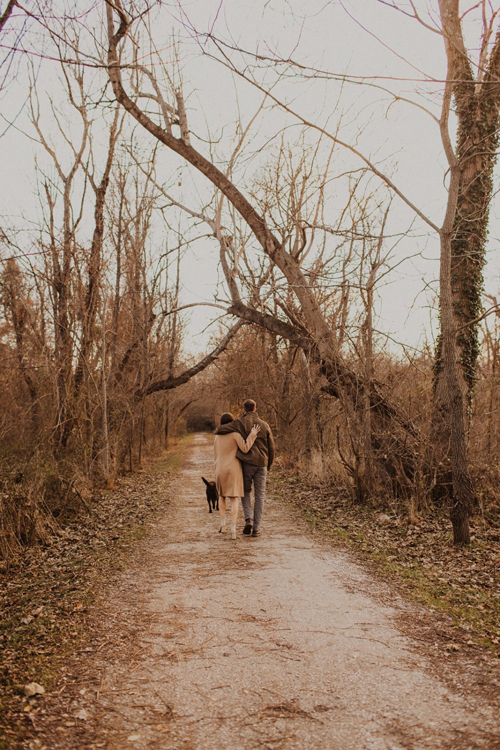 couple walks down trail arm in arm following dog