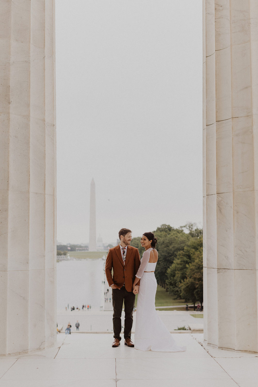 bride and groom embrace beside DC Lincoln Memorial columns