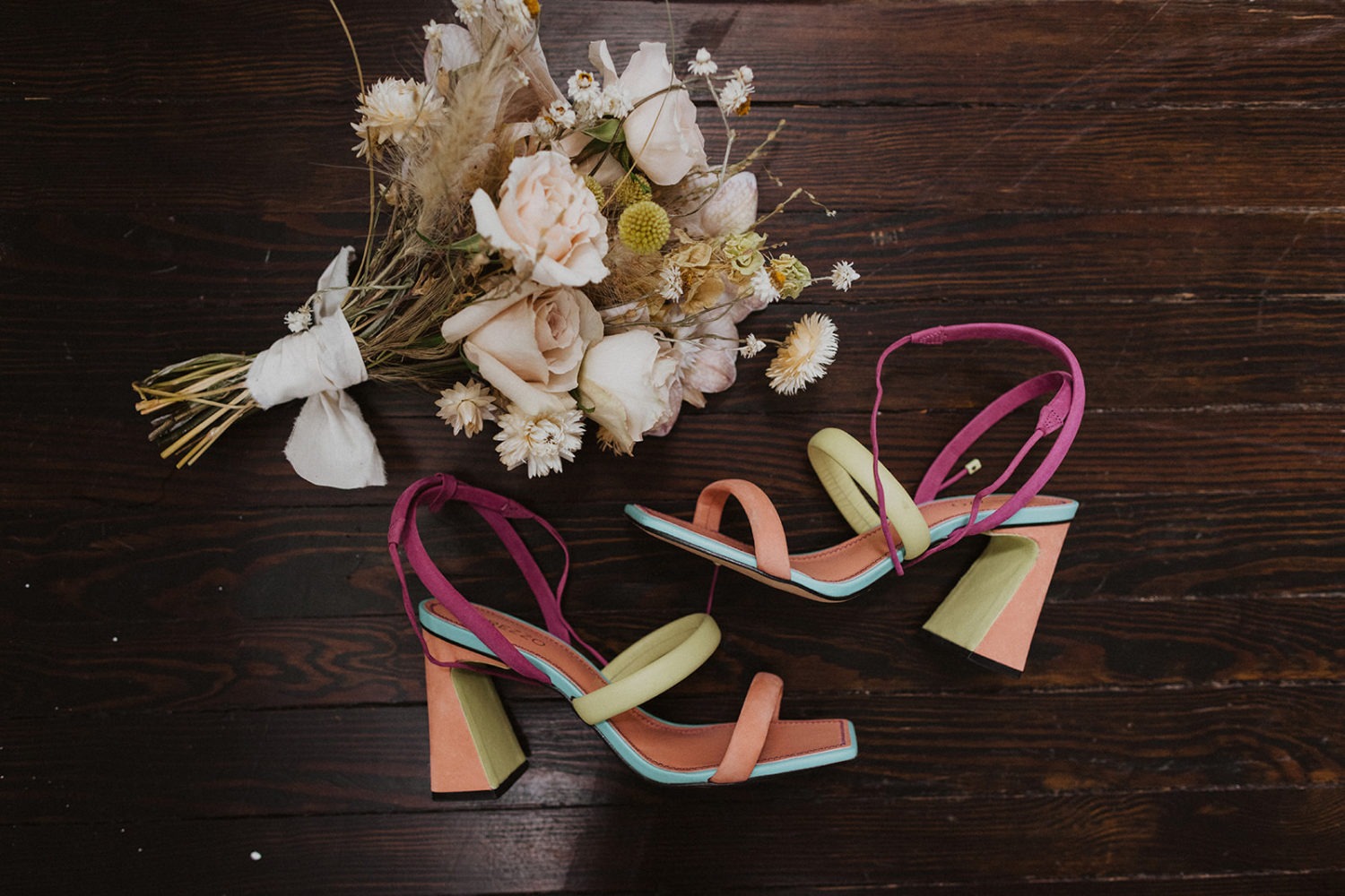 colorful wedding shoes on wood beside white wedding bouquet