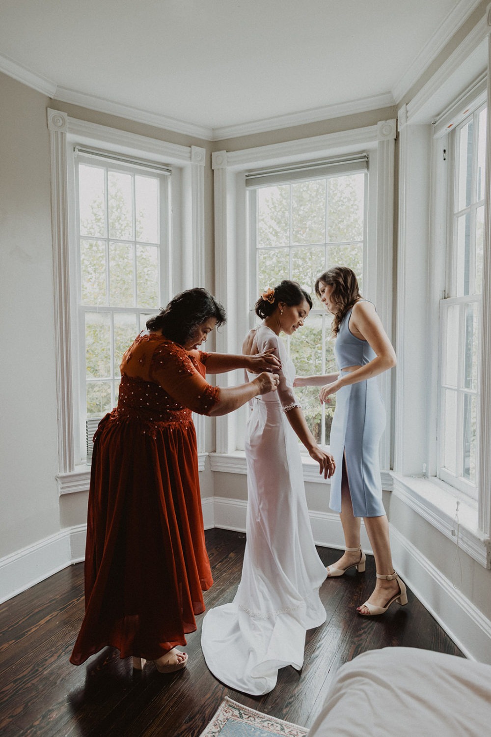 mother of bride helps bride get dressed in wedding dress