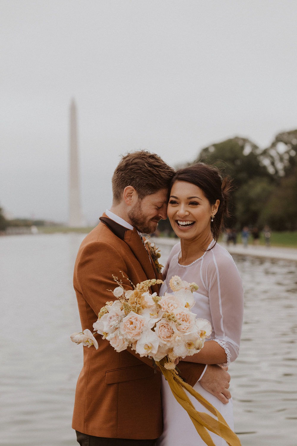 couple embraces holding wedding bouquet standing at the National Mall