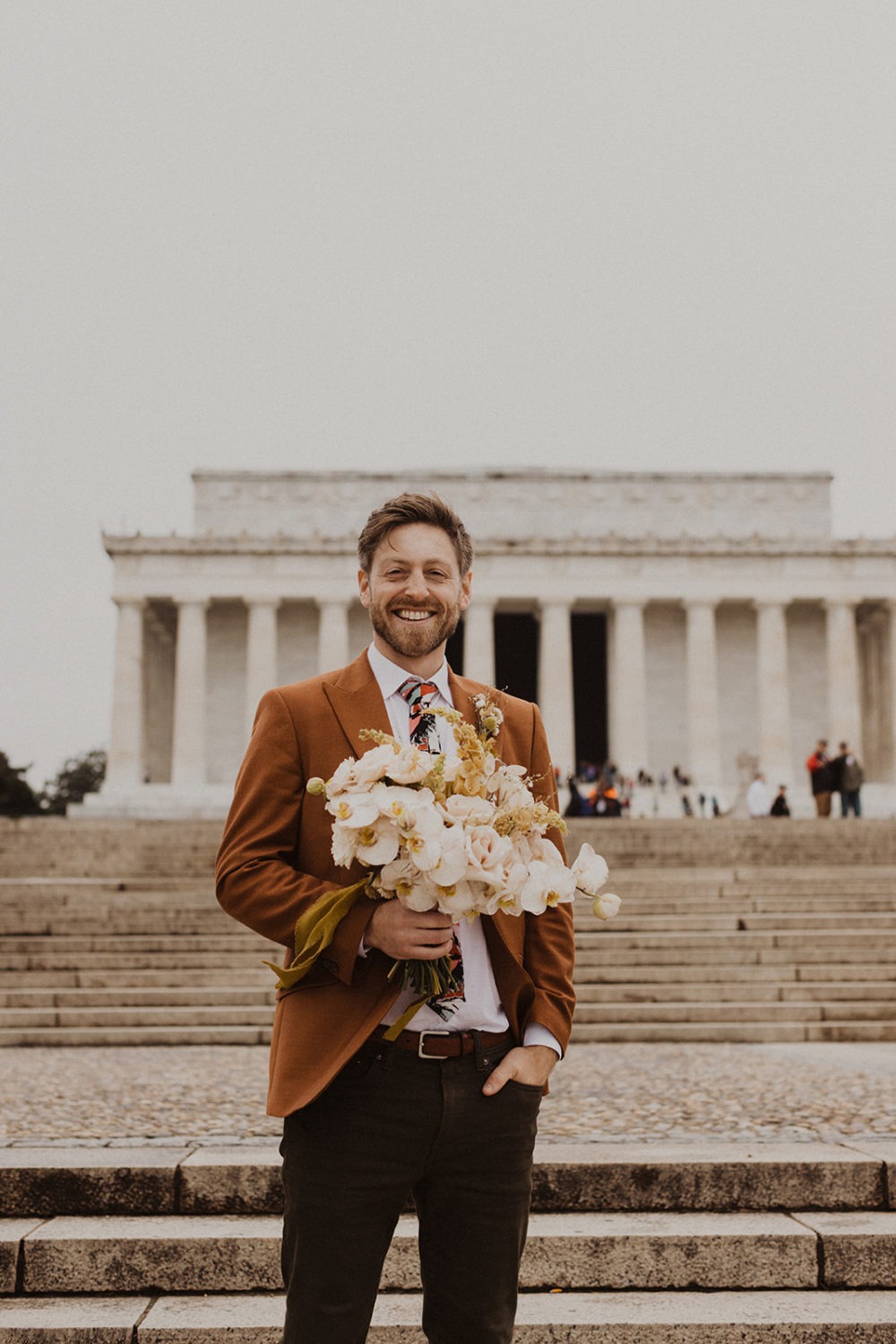 groom stands holding wedding bouquet at Lincoln Memorial