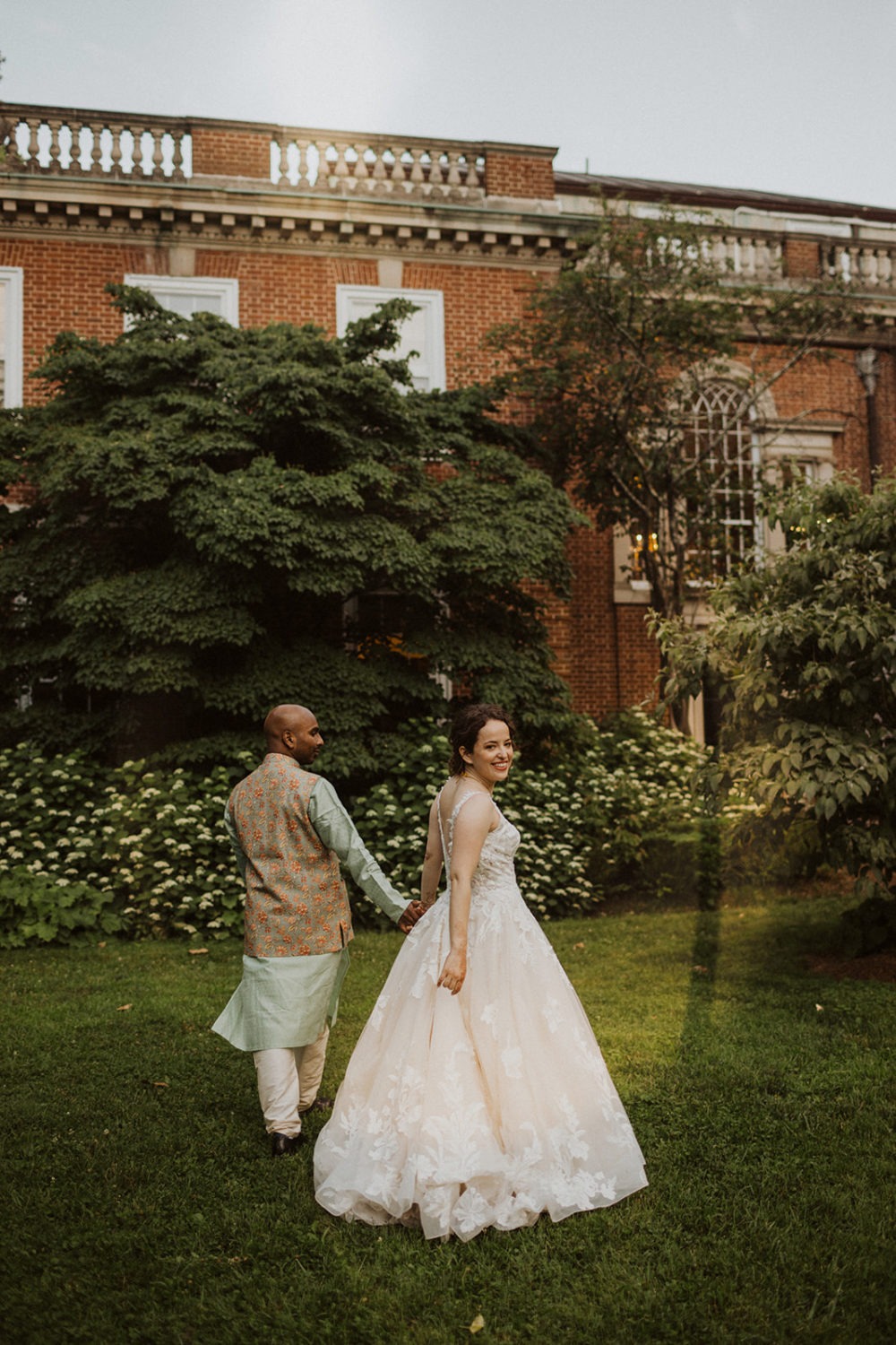 couple holds hands walking through garden at outdoor wedding