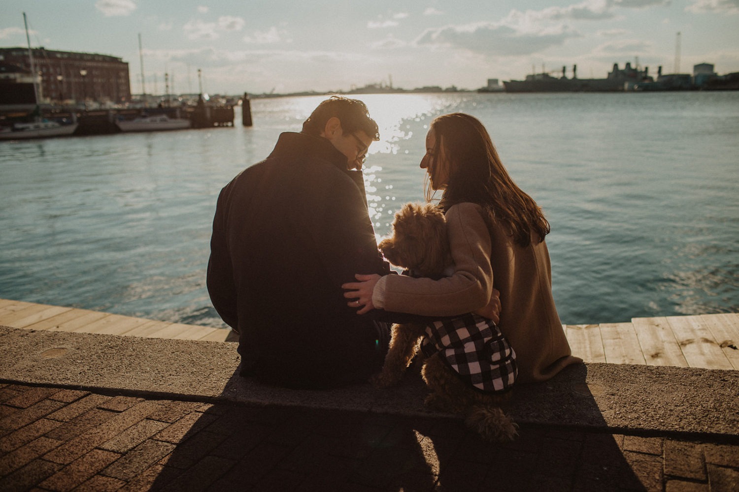 couple sits with dog at waterside Baltimore winter engagement session