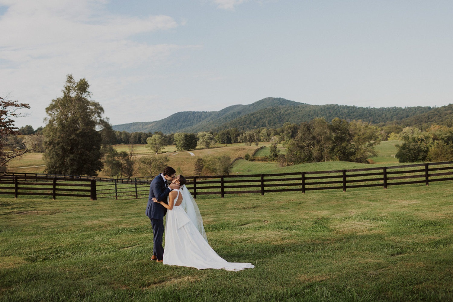 couple kisses in grassy field by mountains at wedding ranch venue