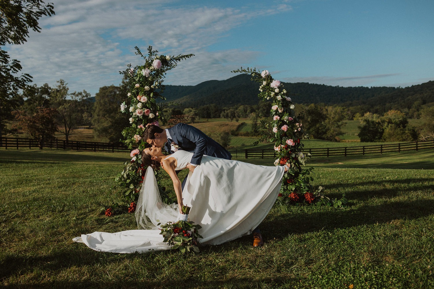 couple kisses under wedding floral arch at mountainside virginia wedding