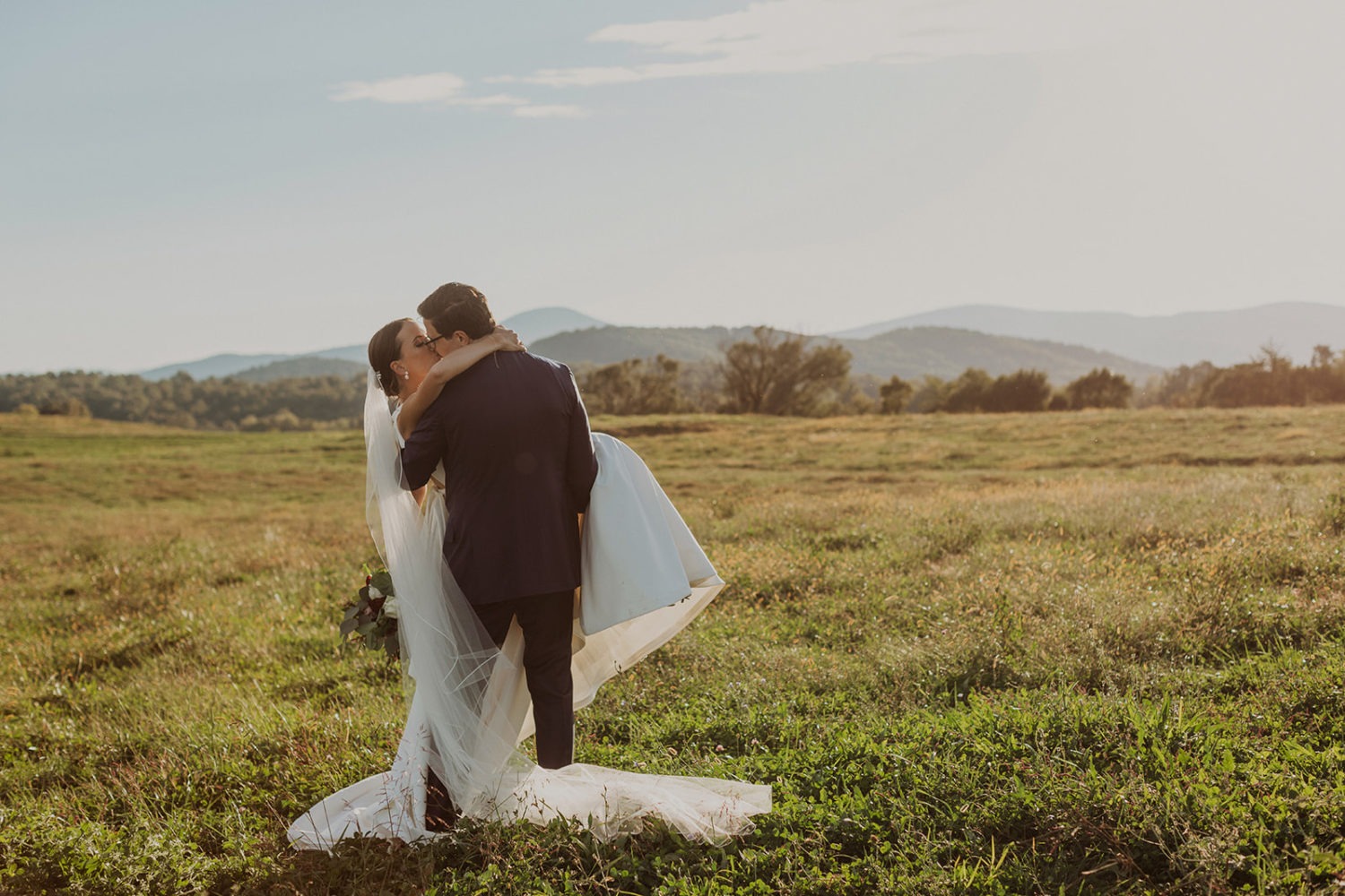 couple kisses in grassy field at wedding ranch venue