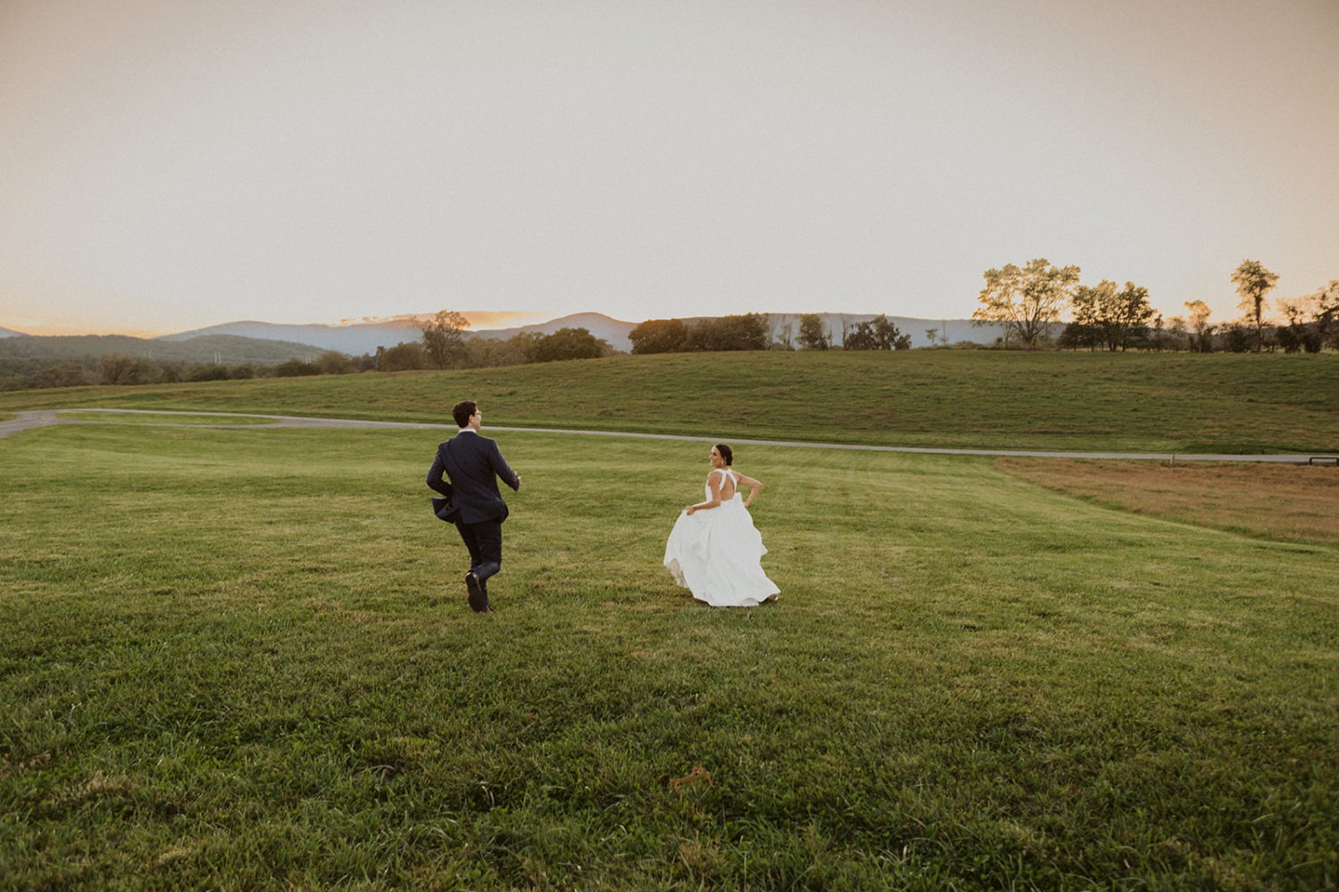 Couple runs through field at sunset wedding ranch venue