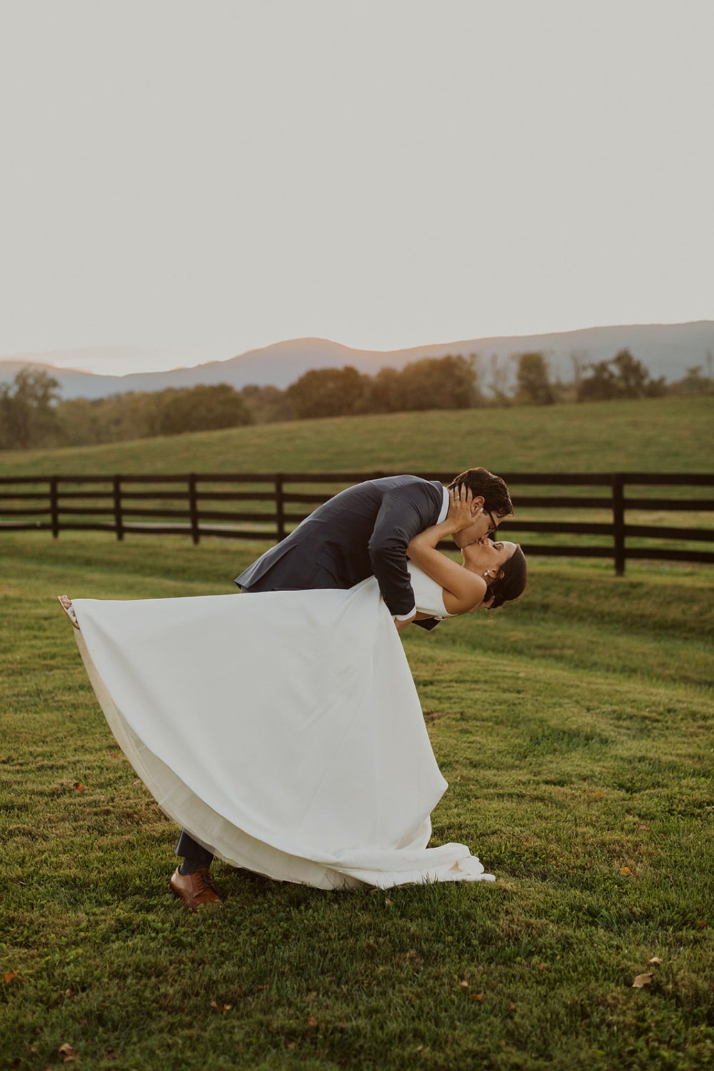 couple bends over for a kiss in field at sunset farm wedding