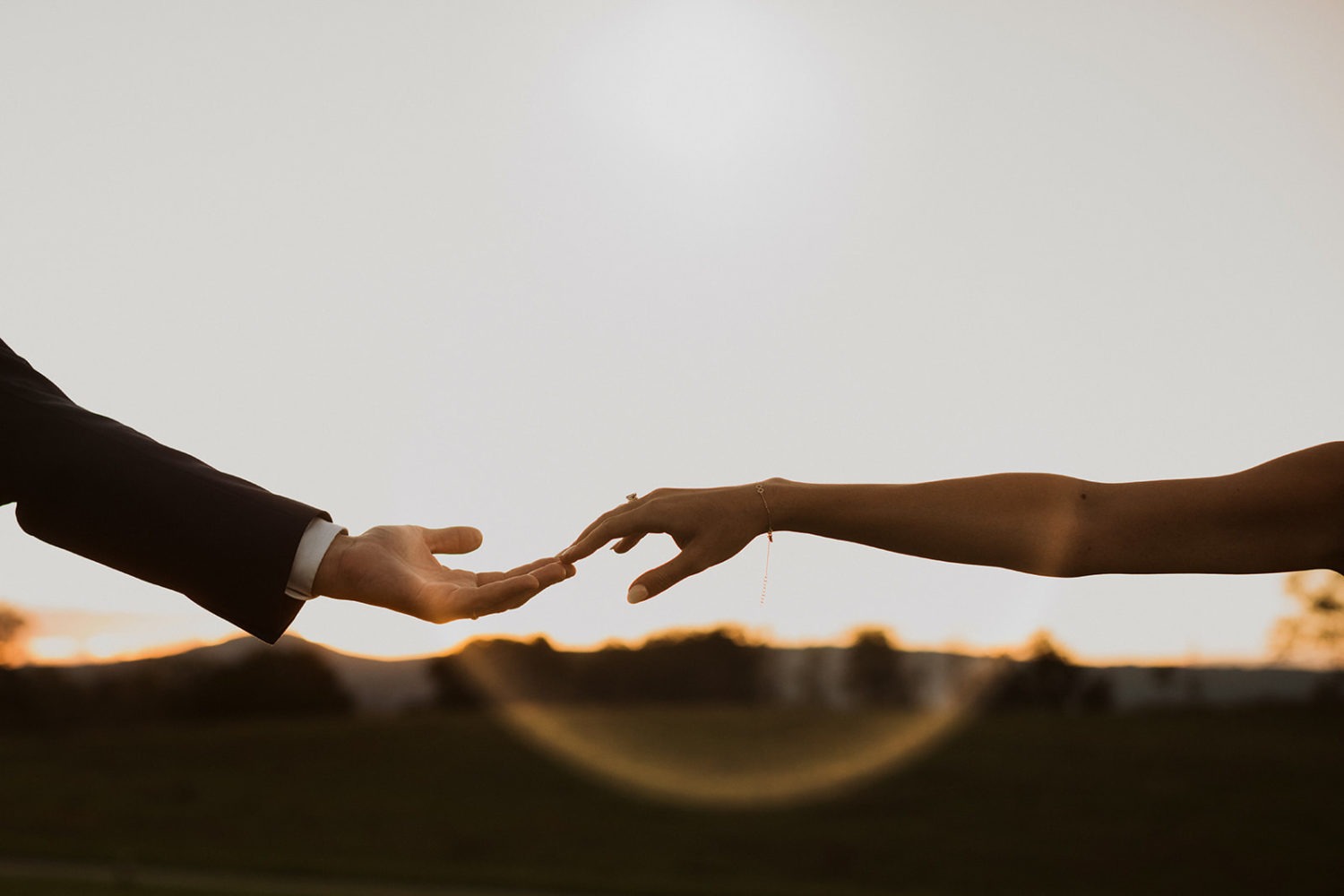 couple reaches for each other's hands with setting sun in background