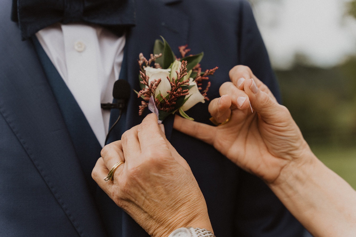 mom attaches boutonniere to groom's suit jacket