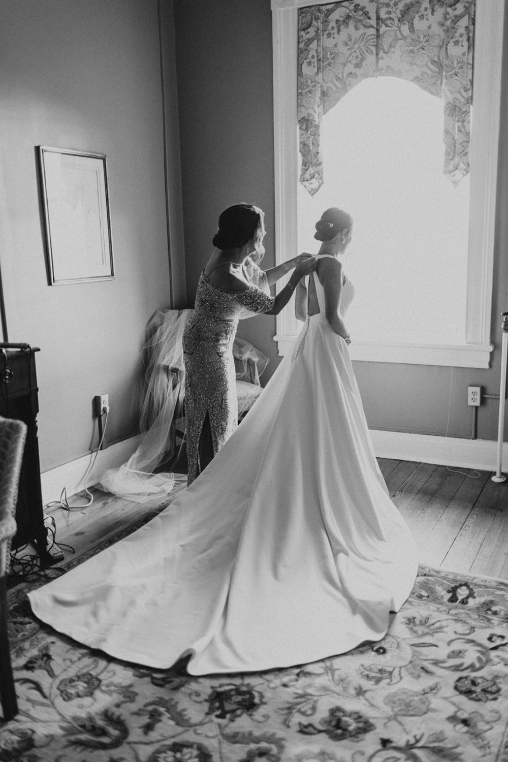 mom buttons up the back of bride's white wedding dress