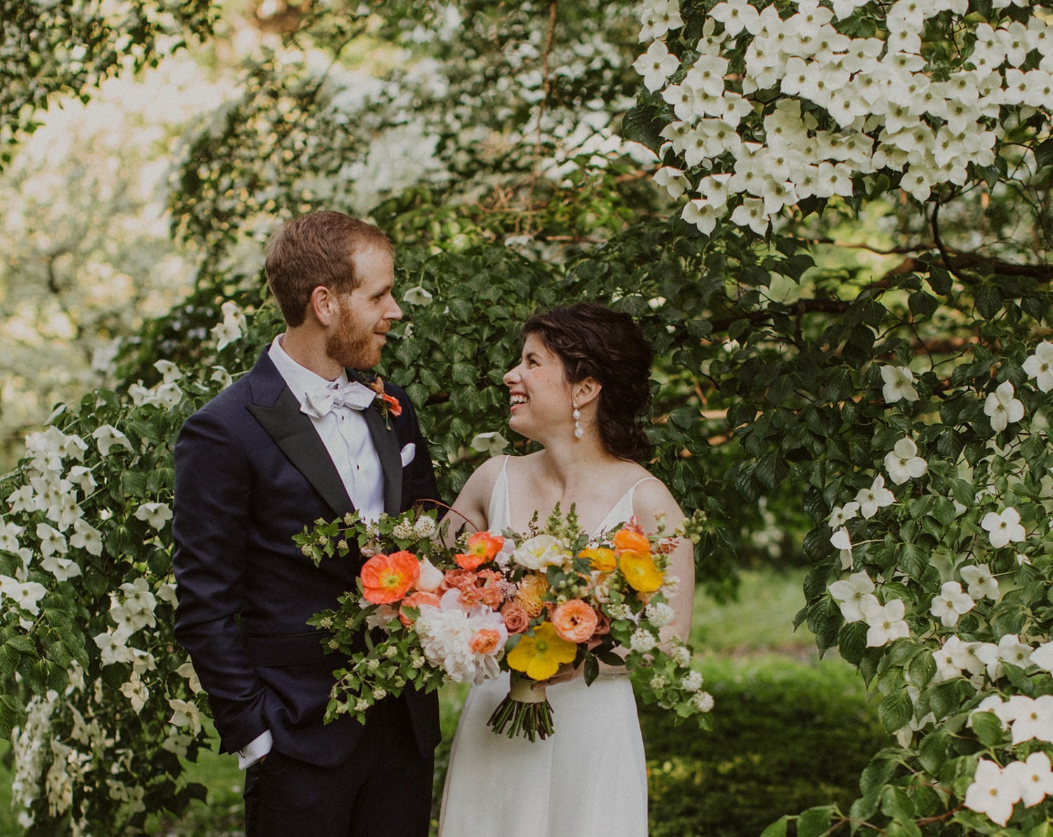 couple laughs surrounded by flowers at garden wedding