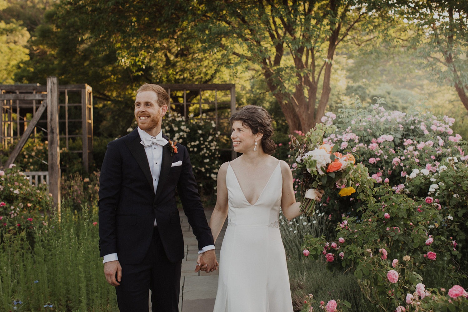 couple walks through garden of flowers at garden wedding