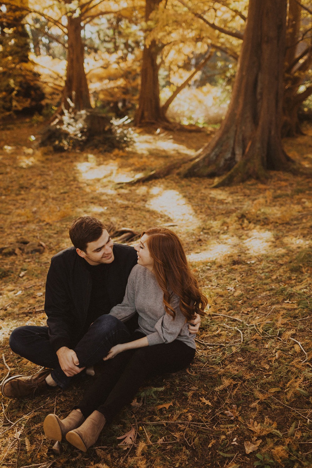 couple sits under trees together at fall sunset engagement