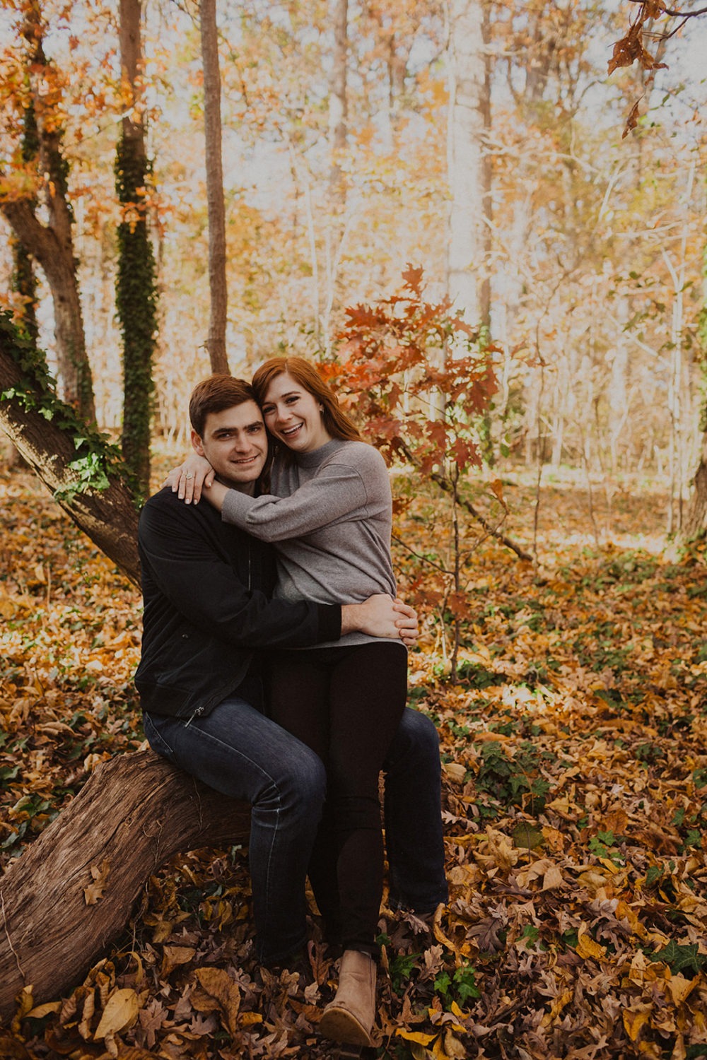 couple embraces seated on fallen tree at sunset fall engagement session