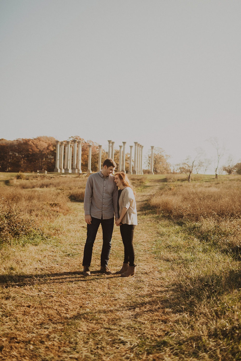 couple stands in sunset fields in front of National Columns at Arboretum engagement