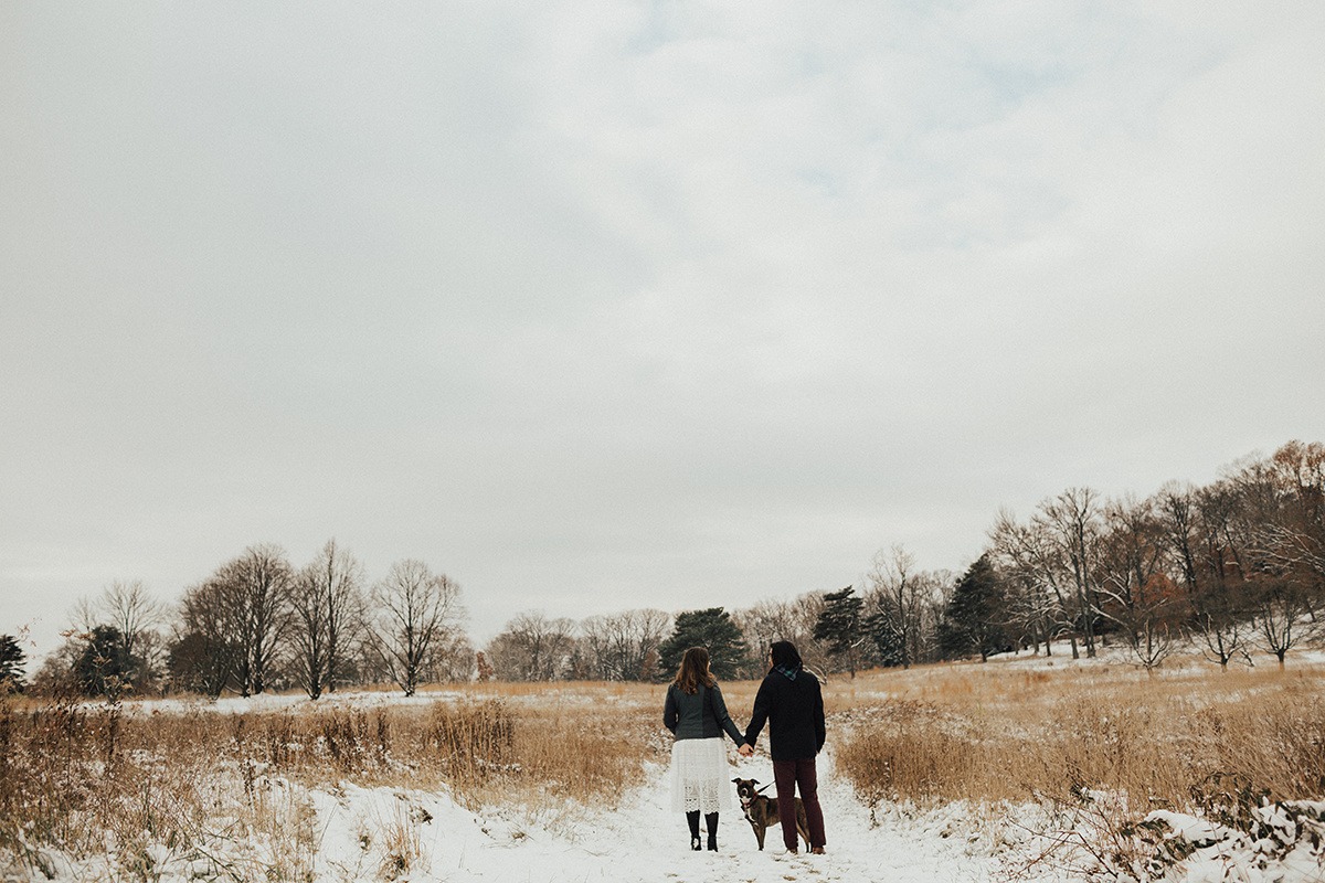 couple walks dog through meadow at winter engagement session