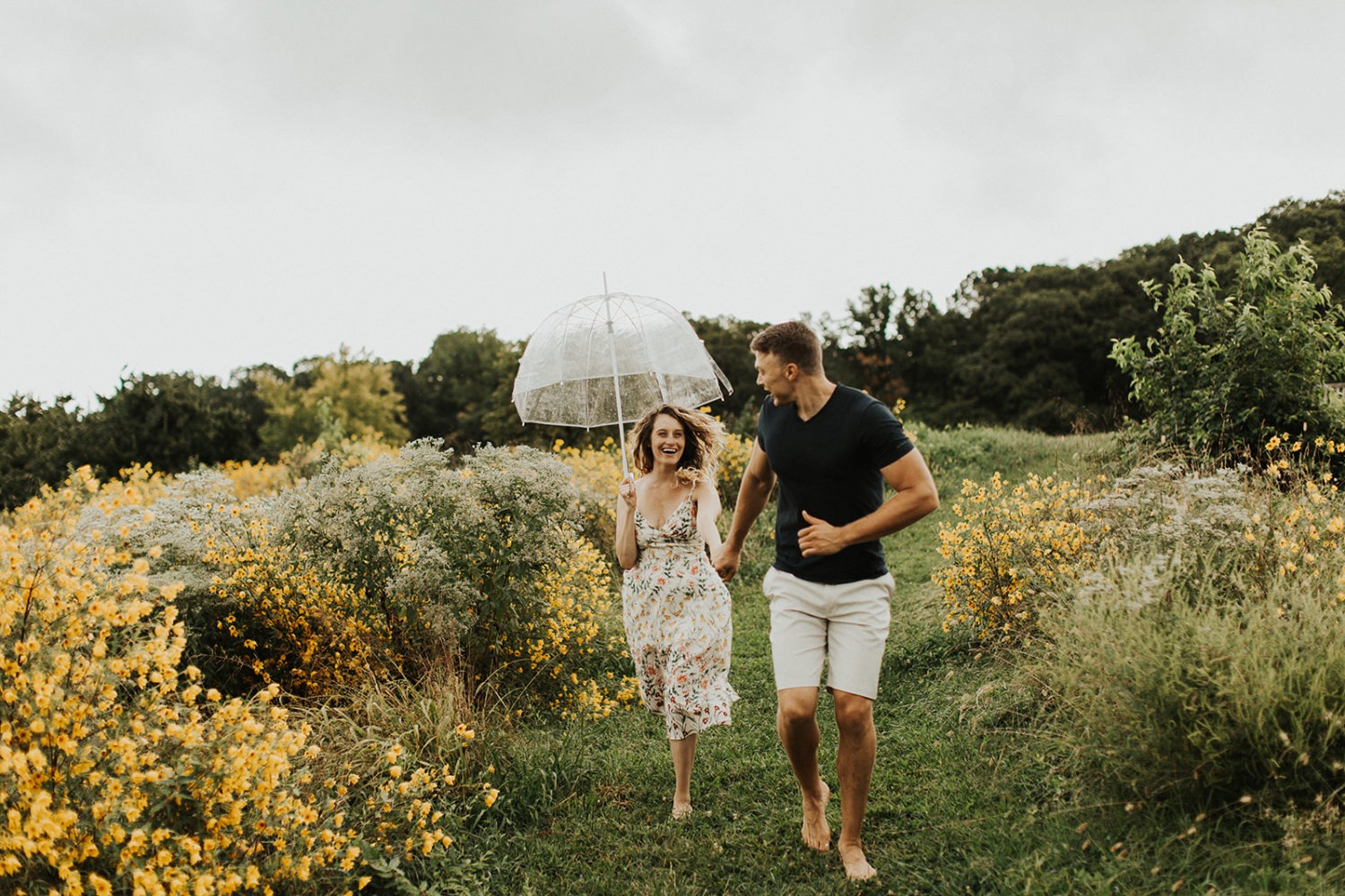 couple runs through meadow of flowers at rainy spring engagement