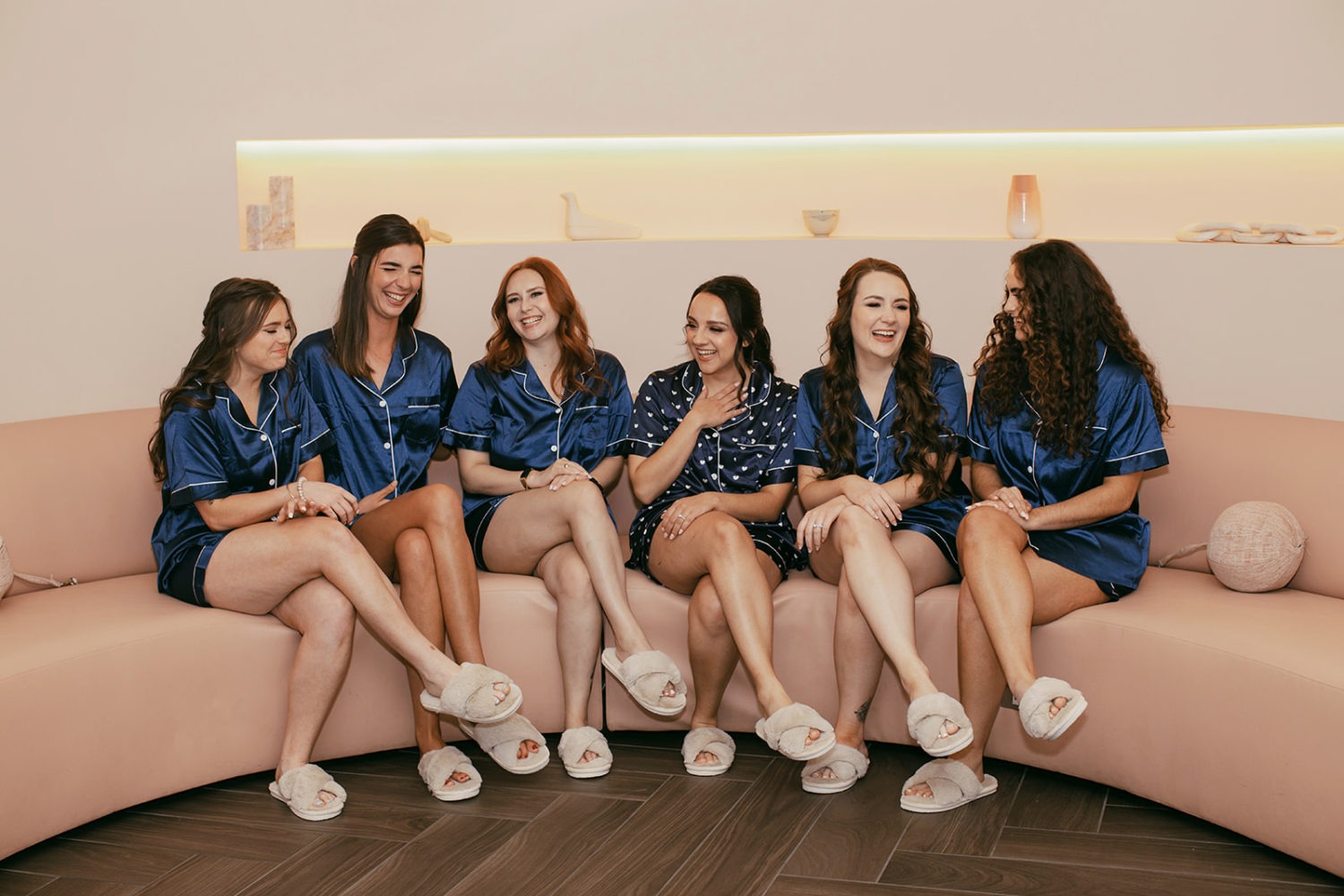 bridesmaids sit with bride on sofa in matching slippers and silk PJ's