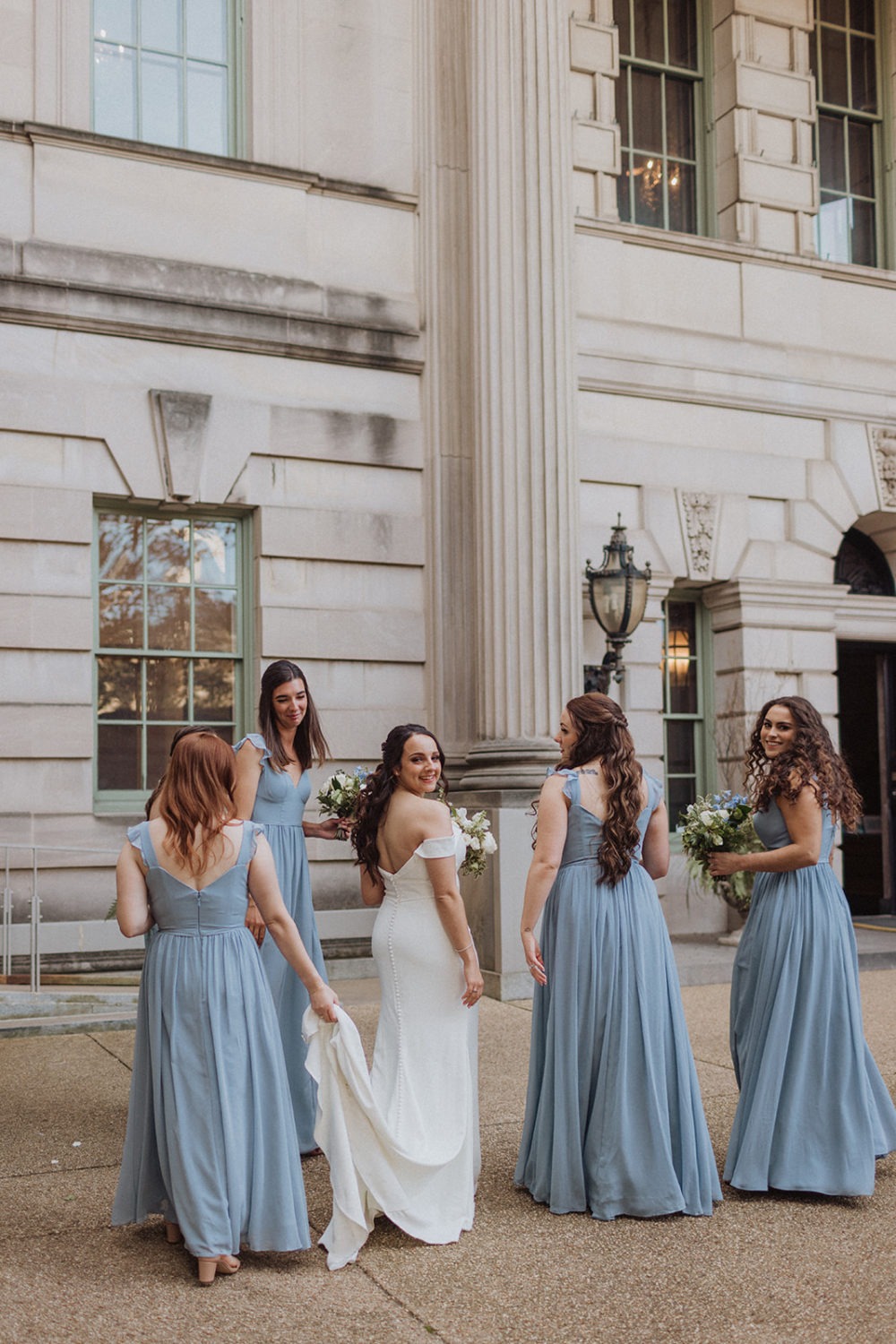 bride walks with bridesmaids under columns at DC mansion wedding venue