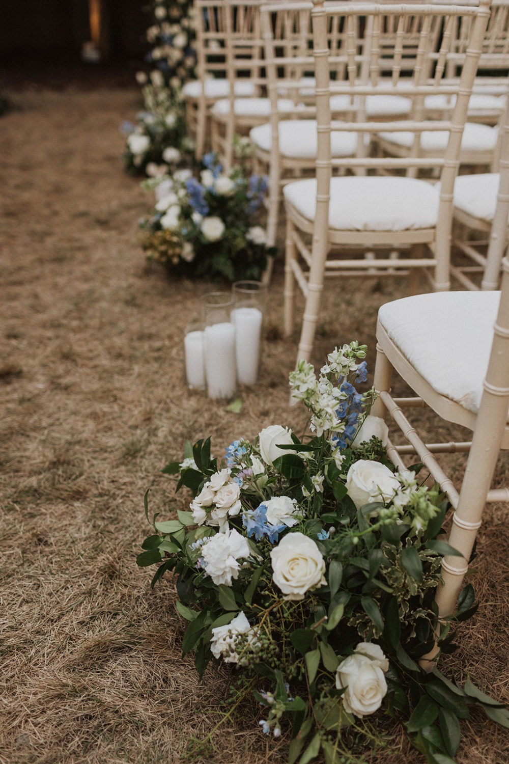 white and blue wedding flowers by white candles at wedding ceremony