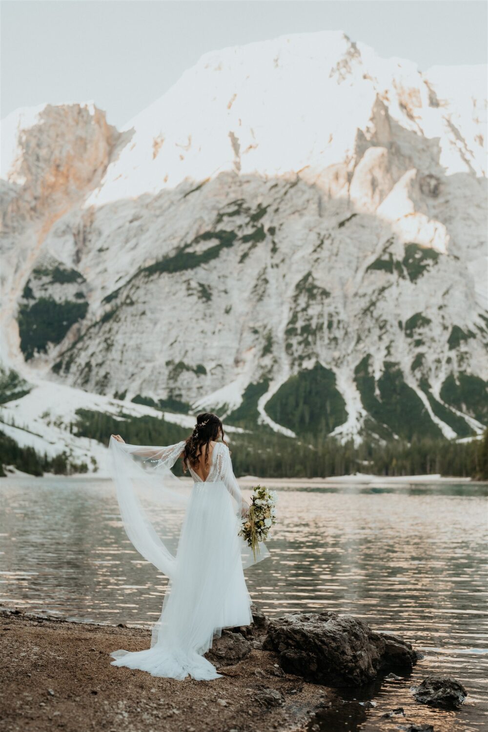 bride holds up wedding dress train beside lake at the Dolomites Italy elopement