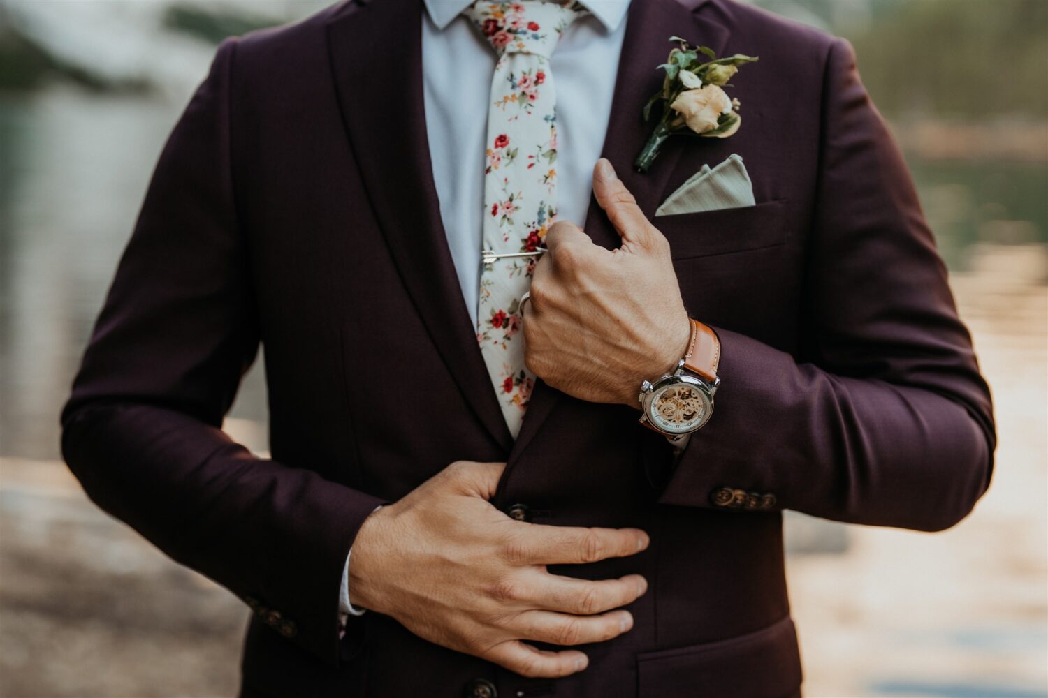 groom holds suit jacket wearing watch and flower tie