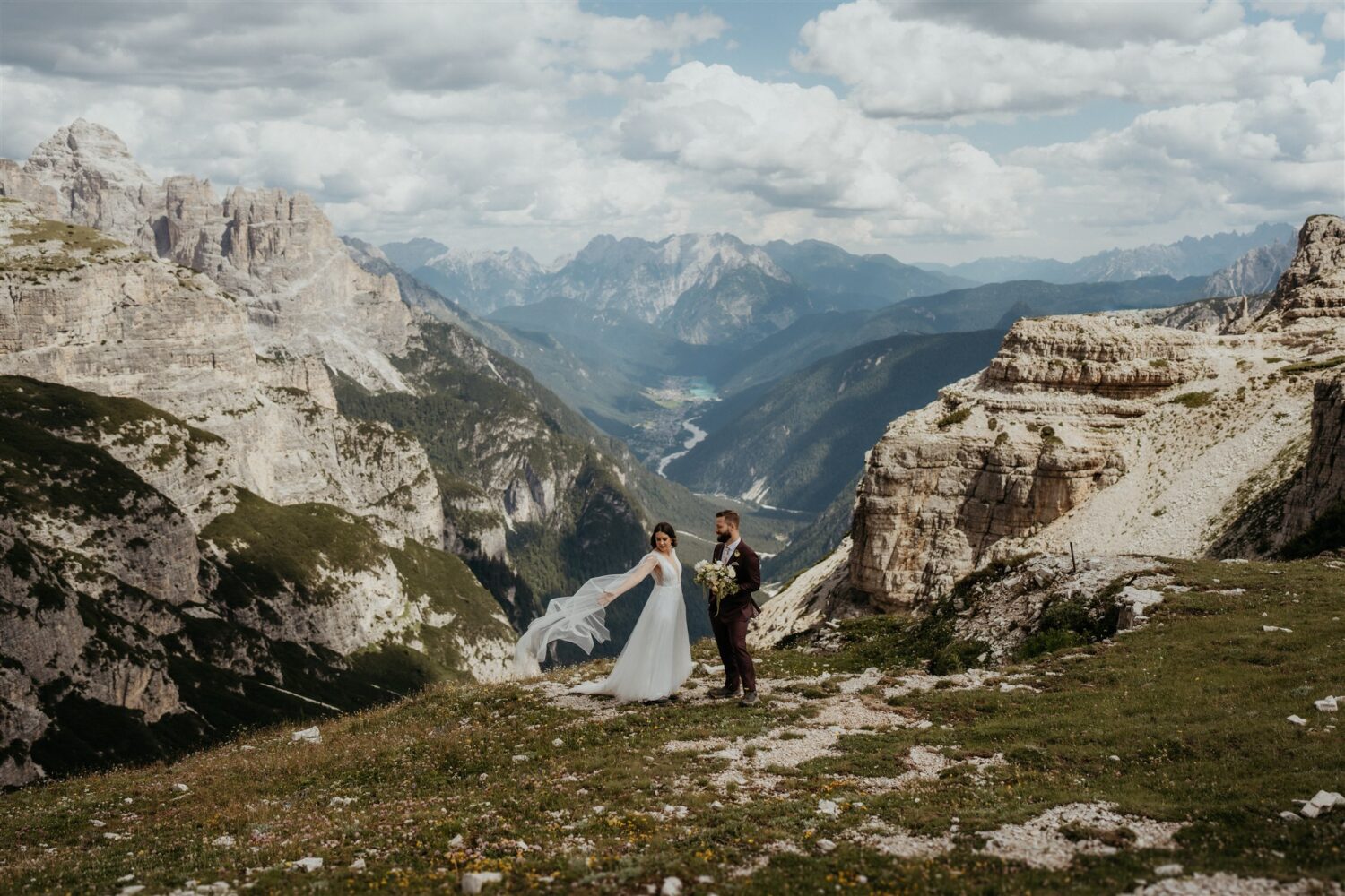 couple stands on mountaintop with wedding train in wind at Italy elopement