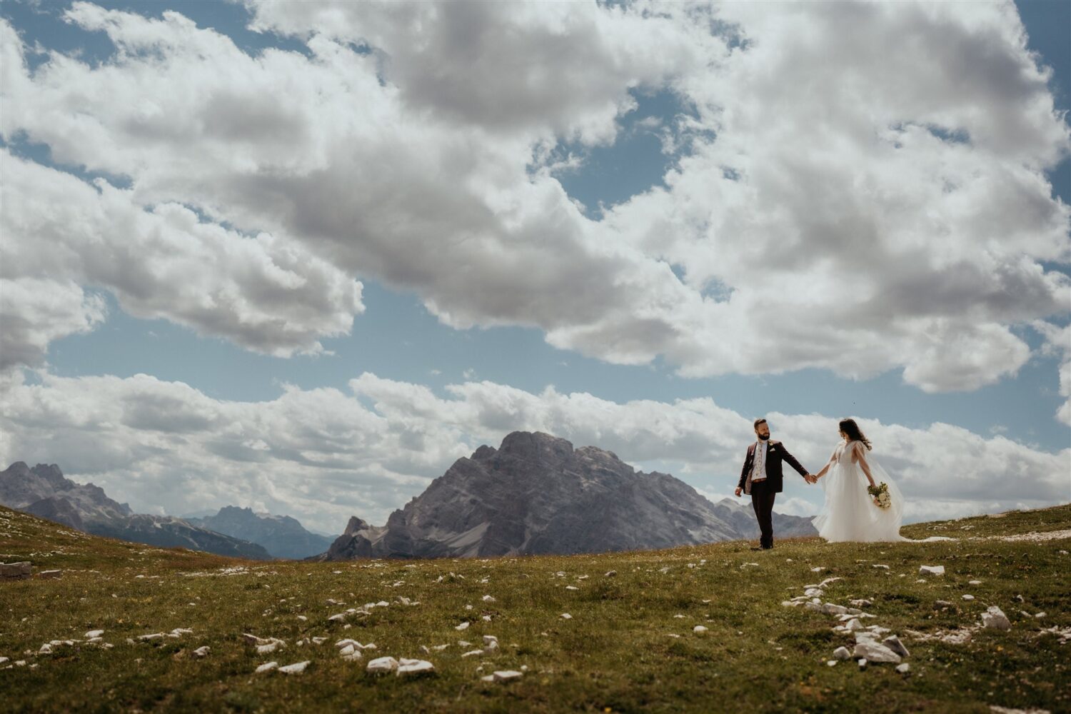 couple walks through grass on mountaintop at Italy elopement