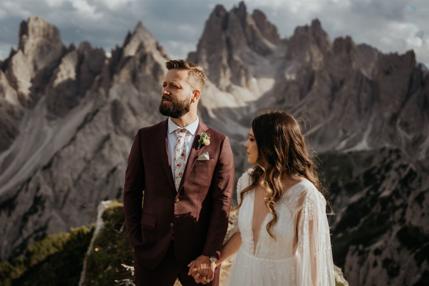 couple holds hands looking away in front of Italian Dolomites