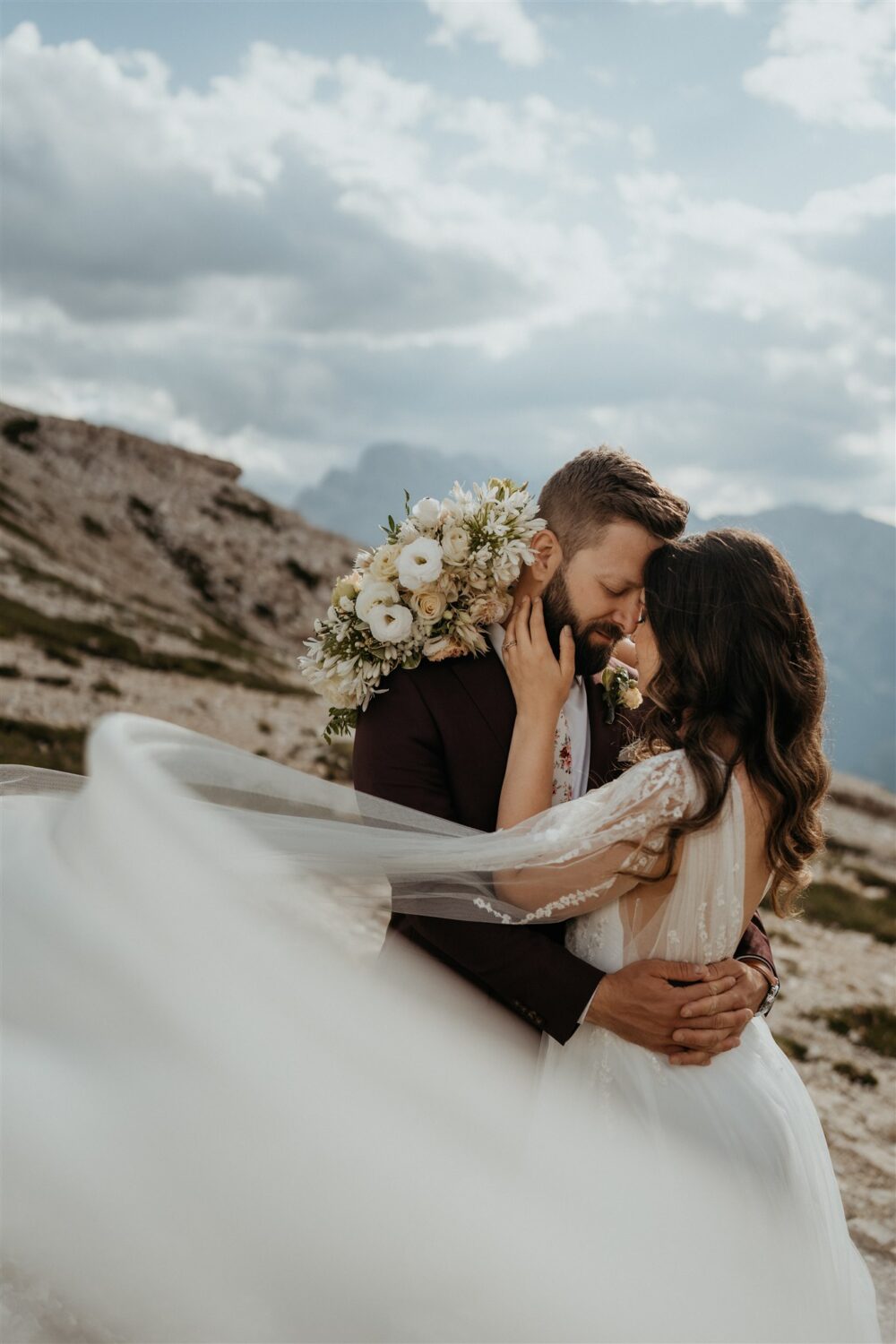 couple embraces with sleeves flowing in wind at mountaintop elopement