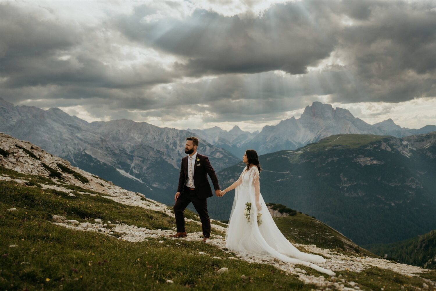 couple walks through grass on mountaintop at Italy elopement