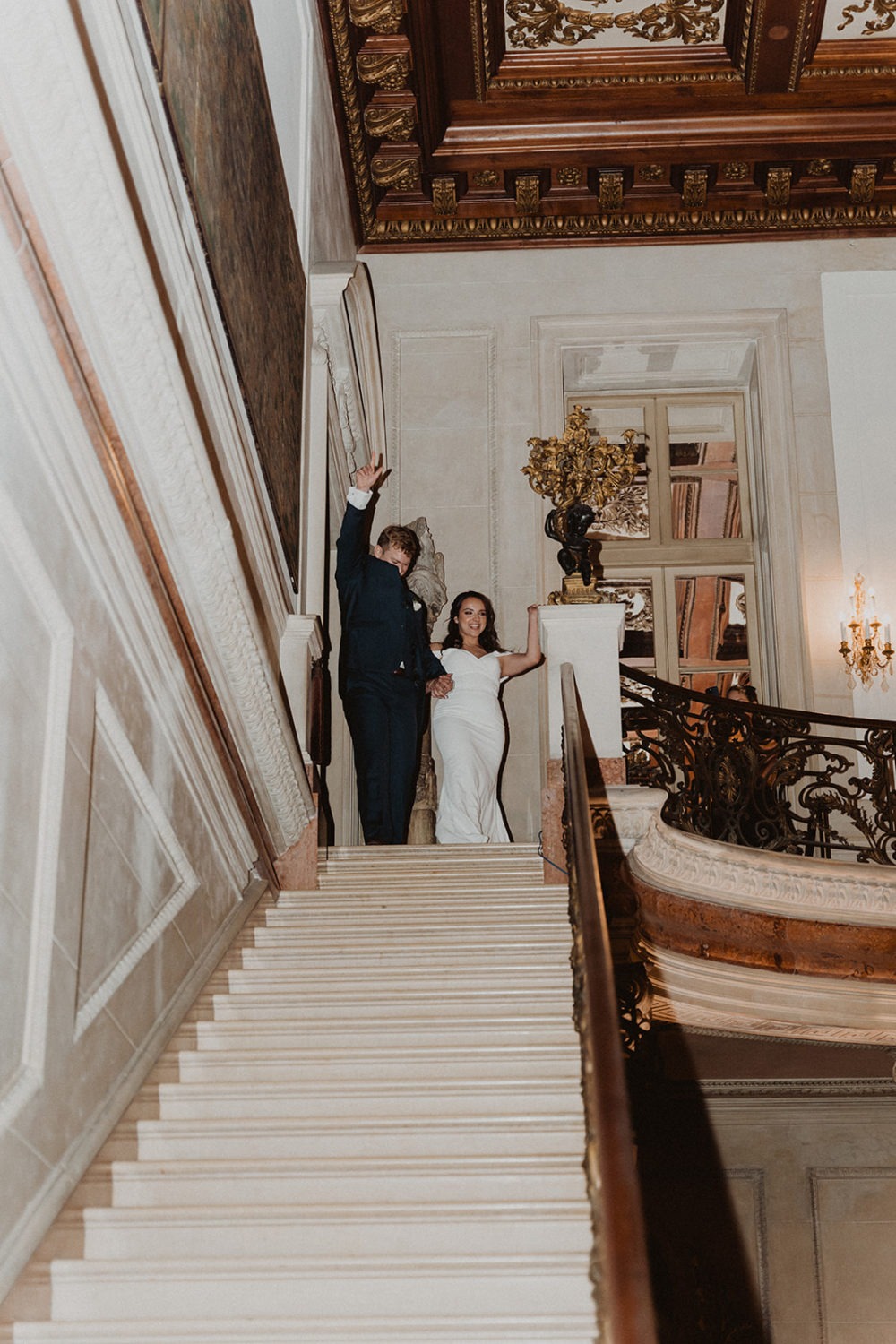 couple walks down grand staircase entering wedding reception