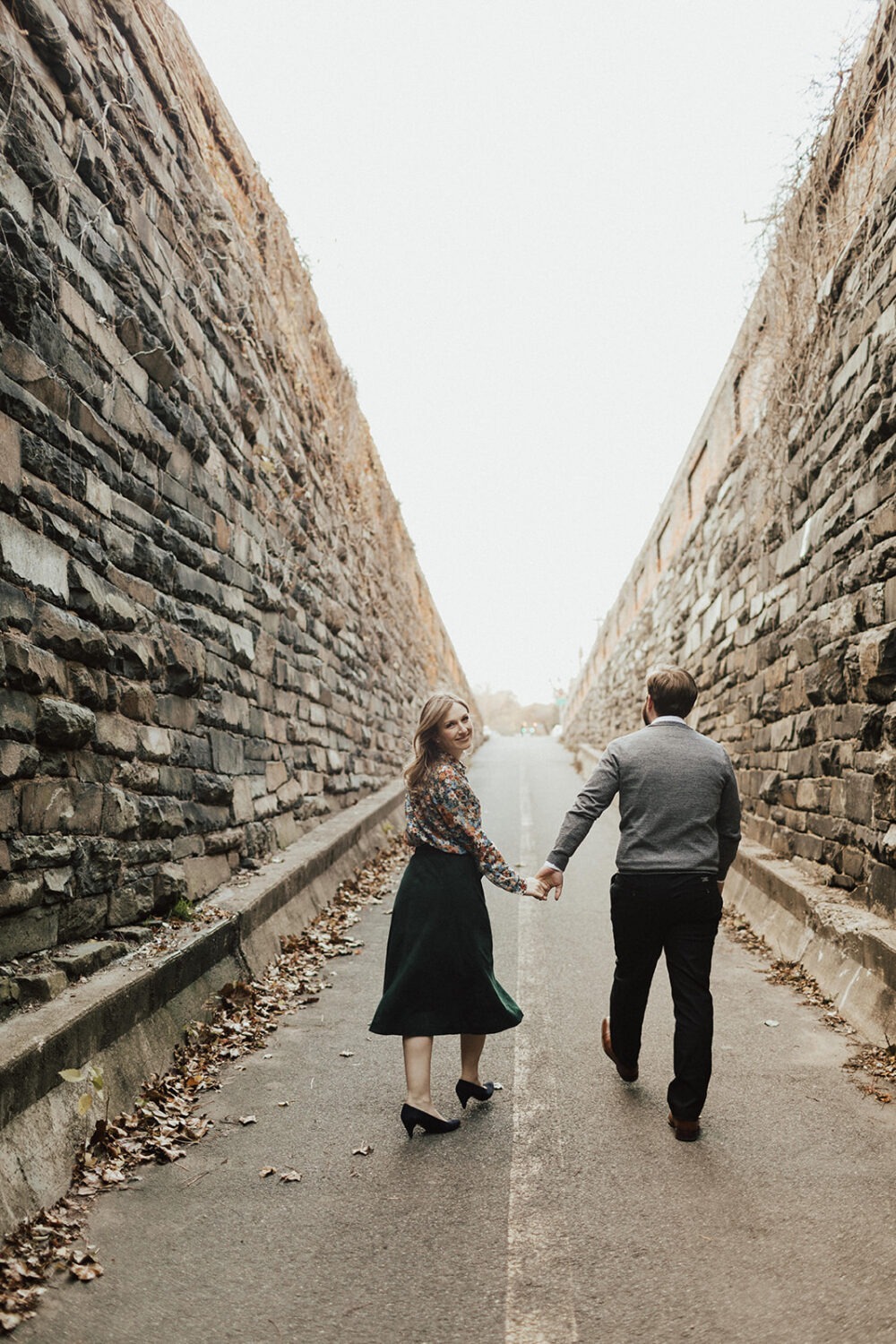 couple walks through stone walls holding hands at engagement session