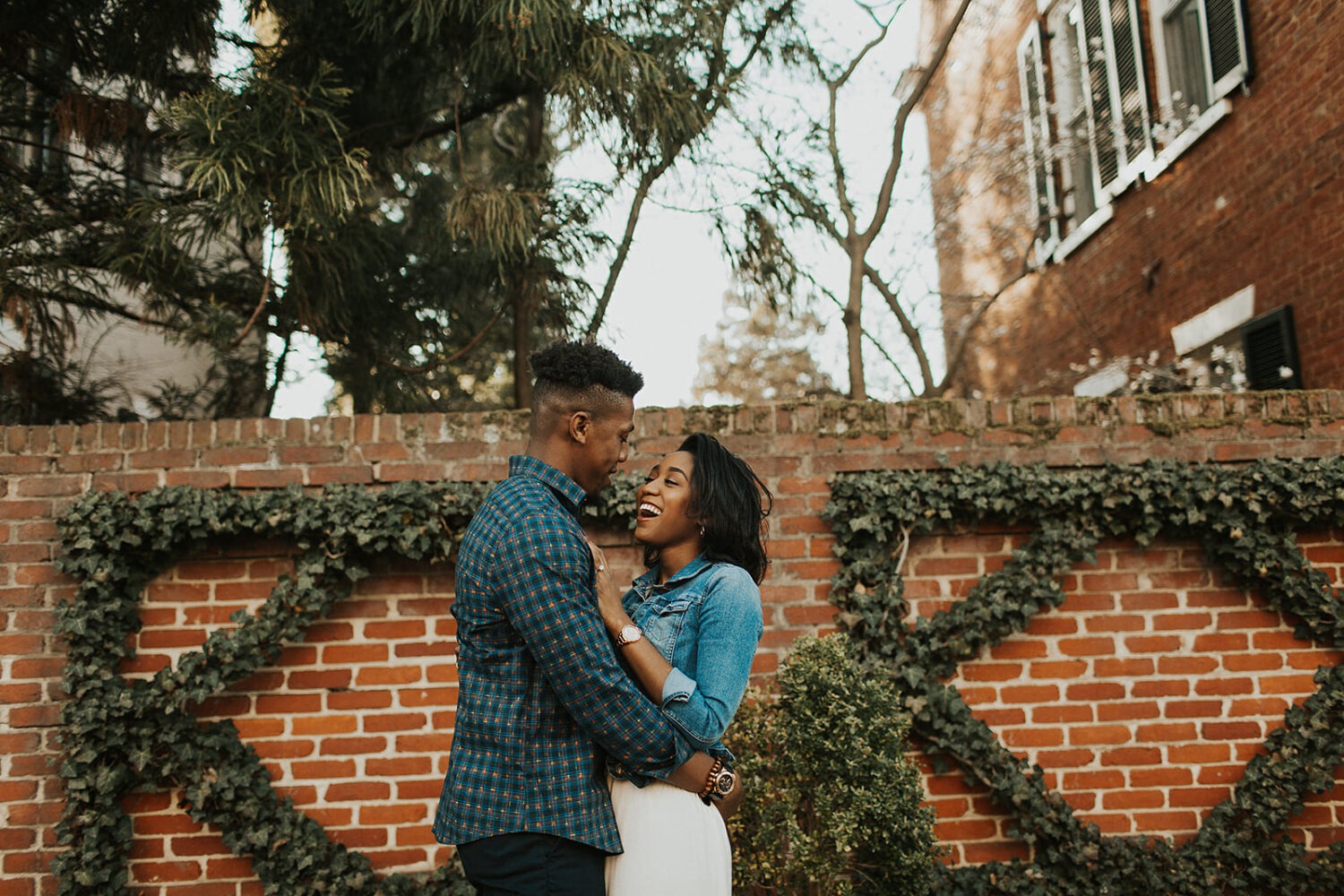 couple embraces in front of ivy-covered wall at engagement session