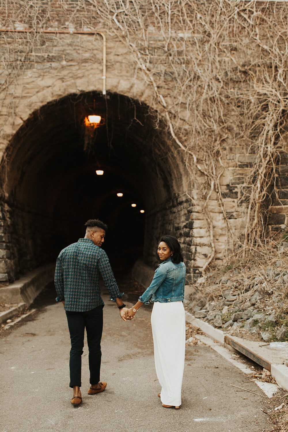 couple approaches ivy-covered tunnel holding hands at engagement session