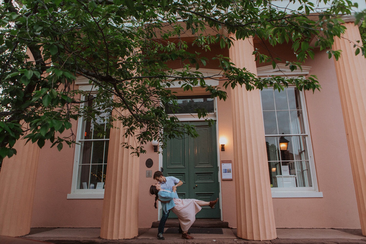 couple stands in front of pink column building at engagement session
