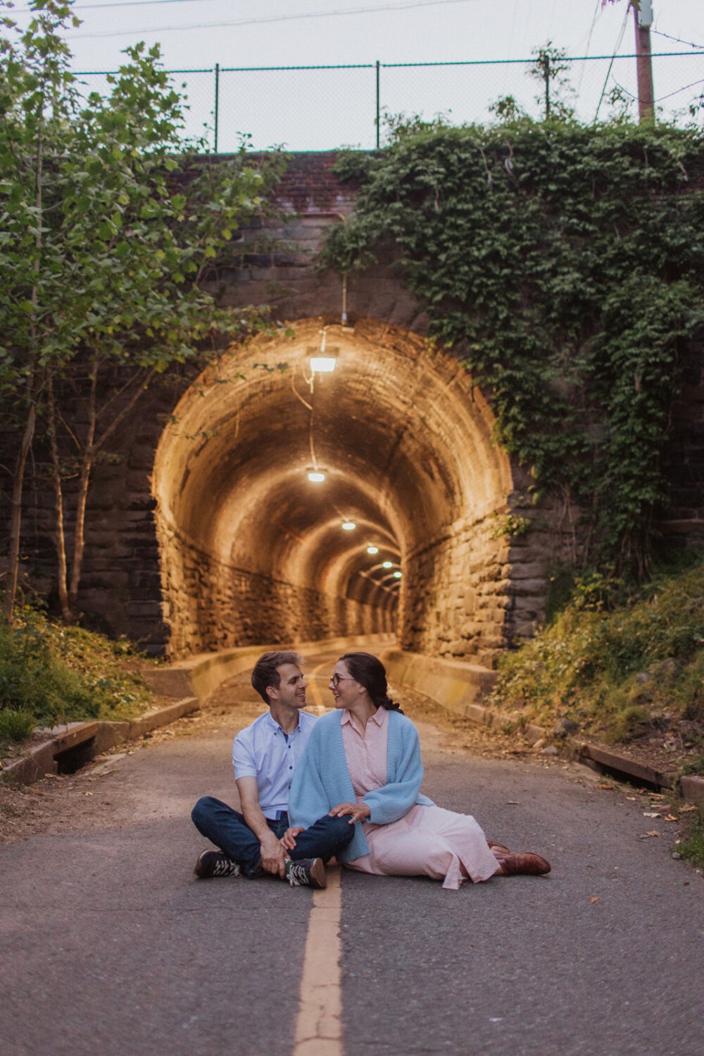 couple sits on ground in front of nighttime lit tunnel