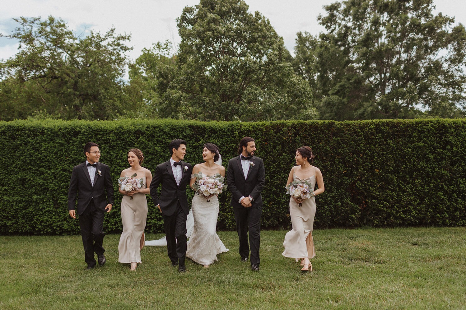 wedding party walks along green hedge at mansion estate