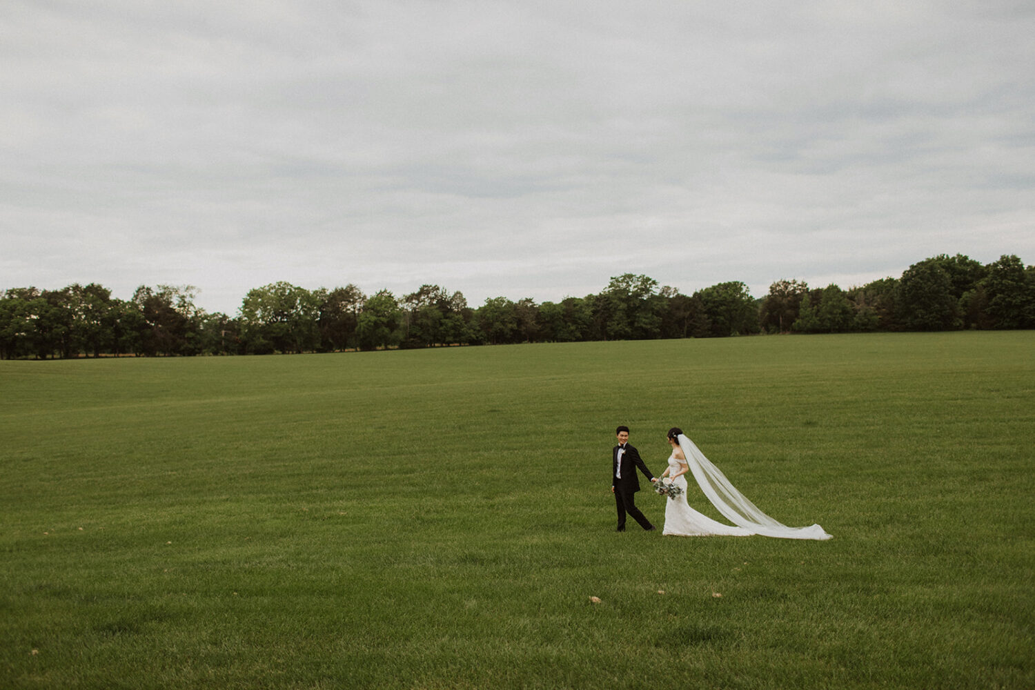 couple walks down through grassy field at Virginia wedding venue