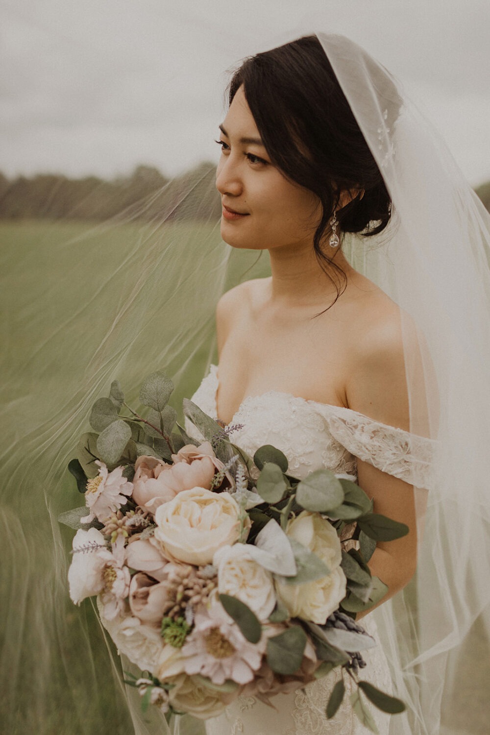 bride holds white flower bouquet under wedding veil 