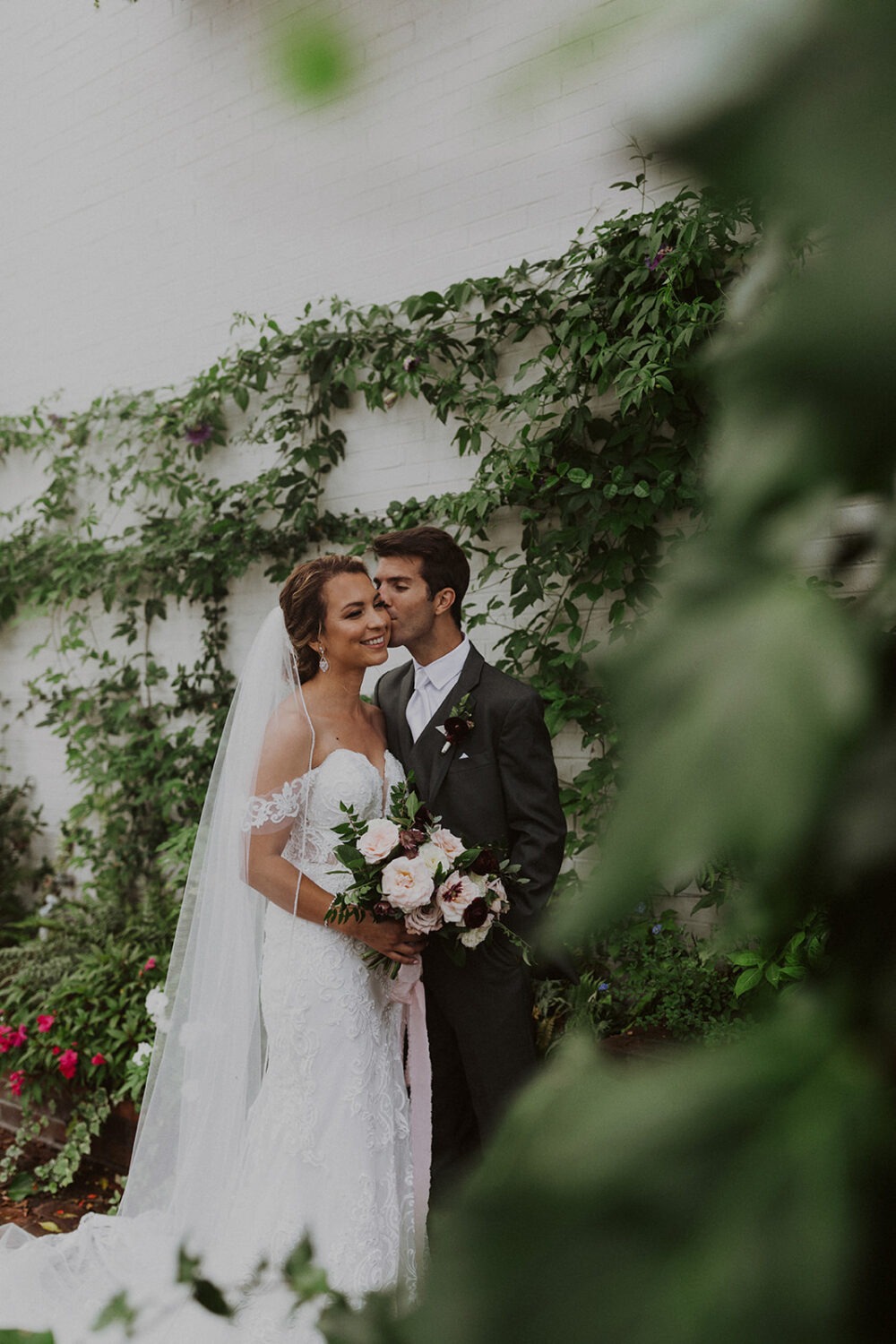 bride and groom kiss beside ivy-covered walls