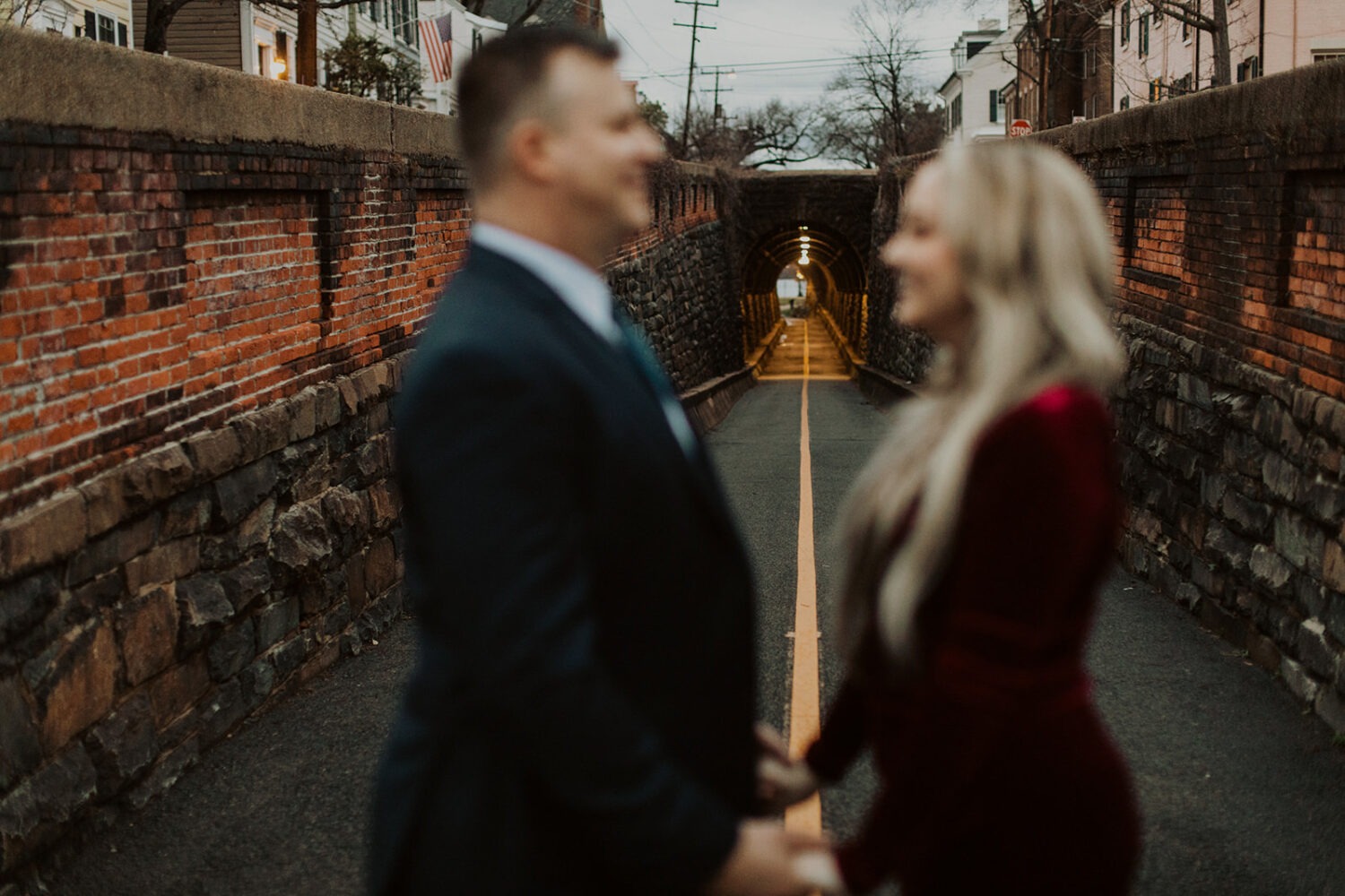 couple stands in front of tunnel at Old Town Alexandria waterfront engagement session