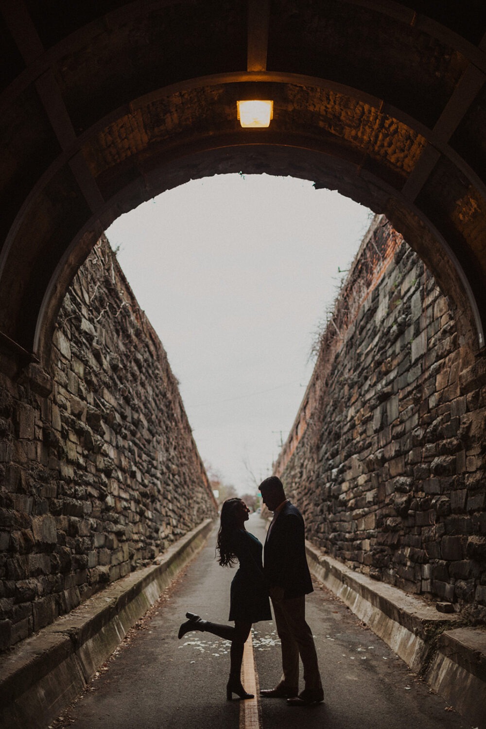 couple stands holding hands in tunnel  at Old Town Alexandria waterfront engagement session