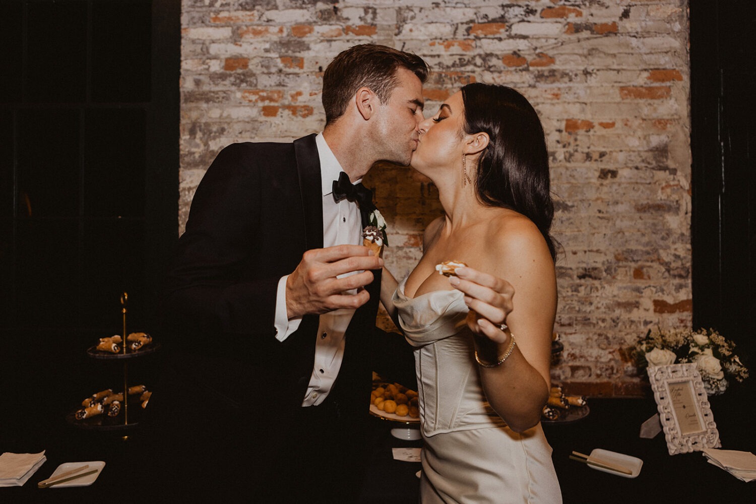 couple kisses while holding dessert at wedding reception 