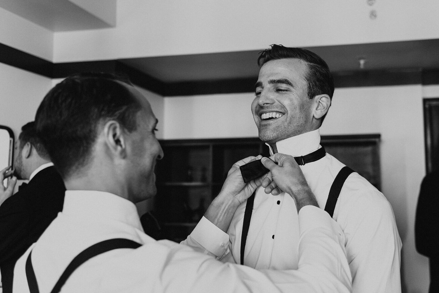 groom has bow tie tied by groomsman at hotel 