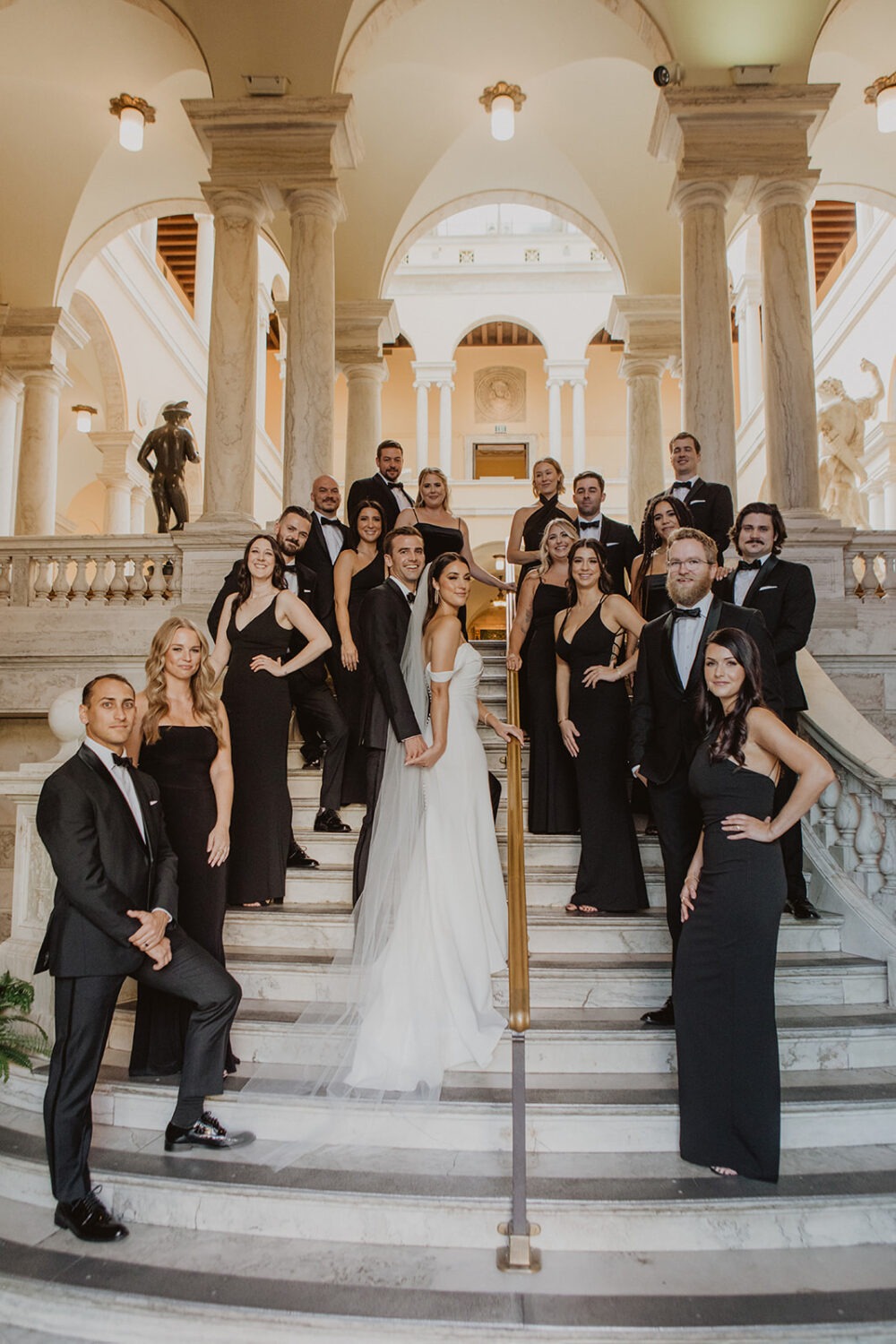 couple stands on marble staircase with wedding party at the Walters art museum 